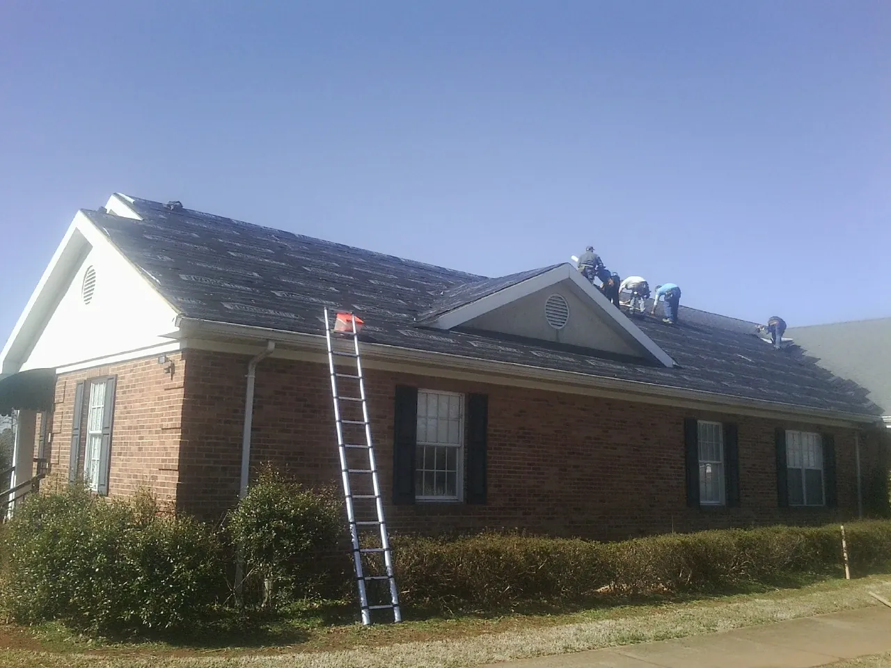 Crew tearing shingles off a brick ranch roof with a ladder set — Metal Roof Repair work by our crew in Litchville