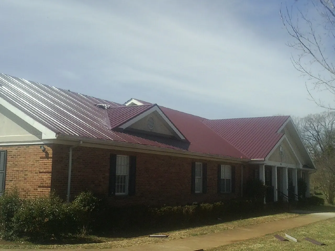 Red metal roof with gabled entries on a long brick building, from a Hail Damage Roof Repair job in Litchville