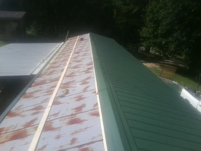 Old rusted panels beside newly installed green metal roofing — Wind Damage Roof Repair by Roofing Brothers in Litchville