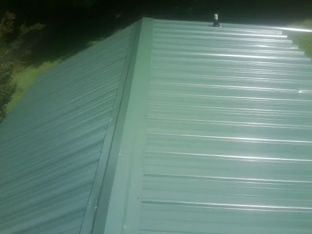 New green metal panels meeting at the ridge of a roof — Flat Roof Repair work by our crew in Litchville