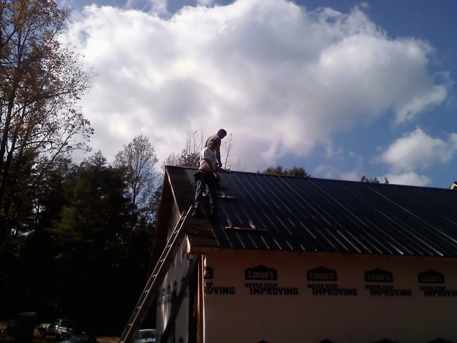 Roofer fastening dark metal panels high against a cloudy sky, from a Roof Inspection job in Litchville