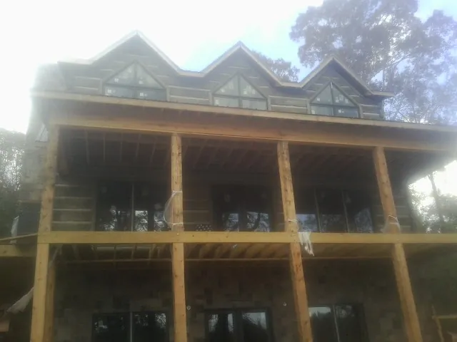 Dormers and porch framing on a large log home under construction — Roof Coating work by our crew in Litchville