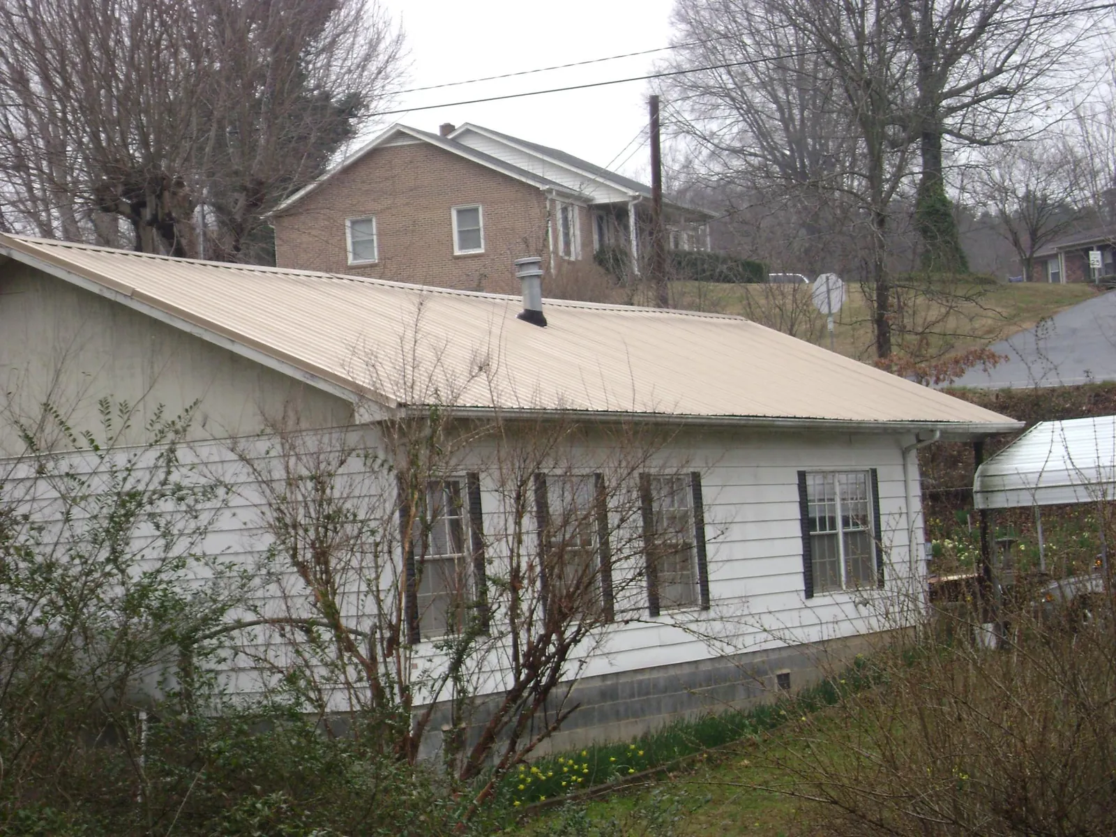 Tan metal roof on a white sided house set into a hillside — Commercial Roofing by Roofing Brothers in Litchville